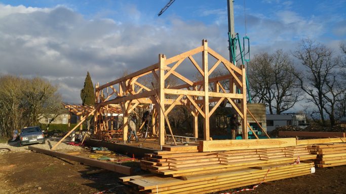 Construction d'une structure en bois avec des poutres apparentes sous un ciel nuageux.