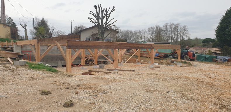Construction d'une structure en bois sur un terrain dégagé. Ciel nuageux en arrière-plan.