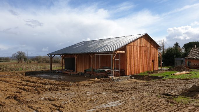 Bâtiment en bois avec toit en pente, situé sur un terrain dégagé.