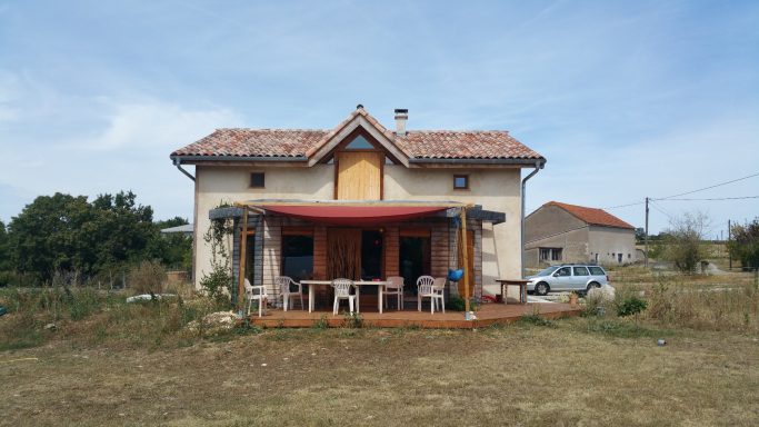 Maison de campagne avec une terrasse à l'avant et un jardin verdoyant.