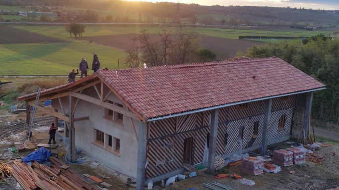 Maison en construction avec un toit en tuiles, entourée de champs.