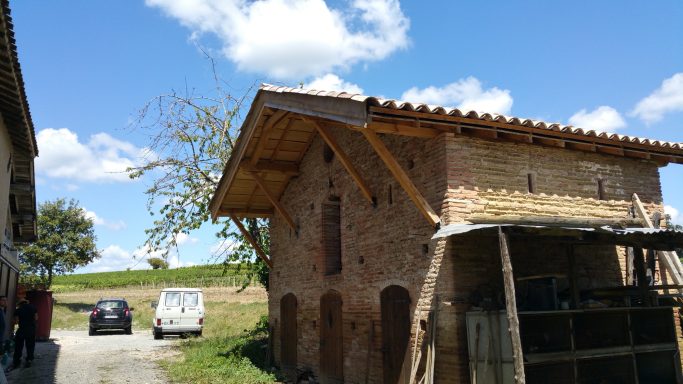 Bâtiment en brique avec un toit en bois sous un ciel bleu parsemé de nuages.
